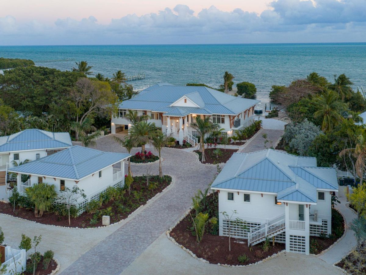 Oceanfront resort with white buildings and blue roofs, palm gardens, and a curving driveway overlooking calm turquoise water at dusk.