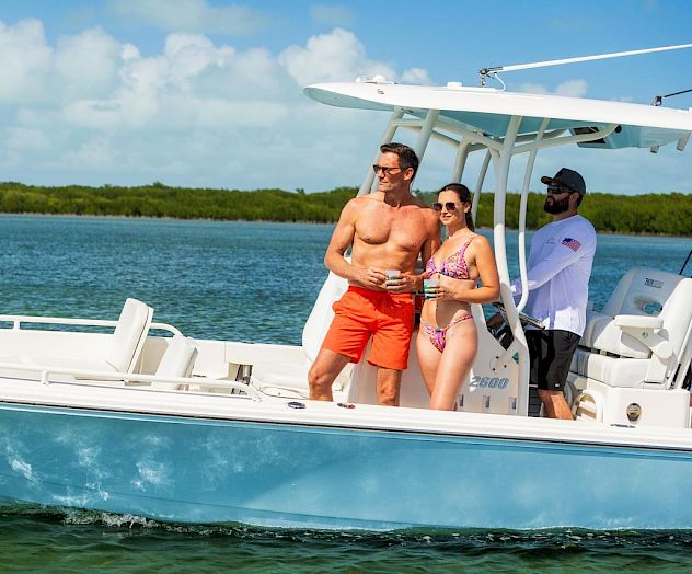 A group relaxes on a sunny speedboat, holding drinks while cruising on bright blue water near a green shoreline.
