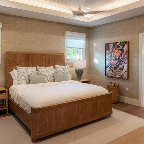 A cozy bedroom with a wooden bed, two bedside tables, warm lighting, a window with curtains, a dresser, and a small seating area in a classic style.