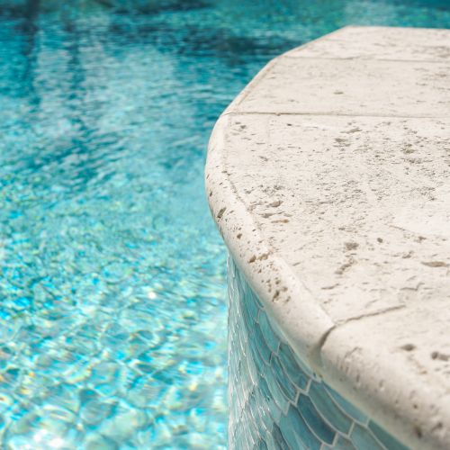 A pool with bright blue water, a curved beige edge, and sunlight reflecting off the surface.