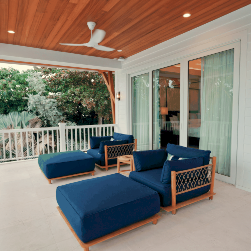 A bright, modern living room with a blue sofa, white walls, and natural light streaming in from large windows, styled with plants and warm decor.