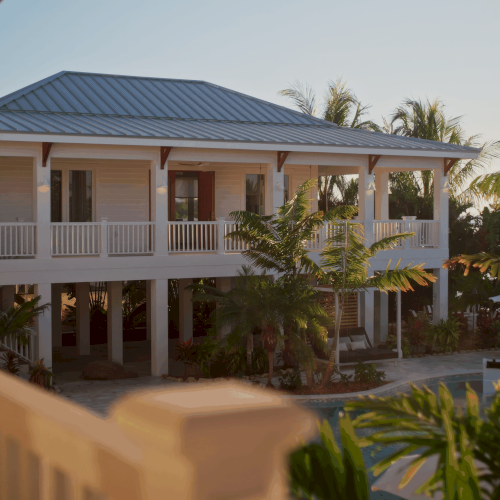 A sunny coastal resort with beige and white buildings, balconies, palm trees, and bright blue sky, inviting outdoor warmth.