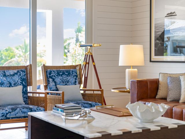 A bright living room with blue chairs, a leather sofa, a marble coffee table, and a brass telescope-style decor on a tripod.