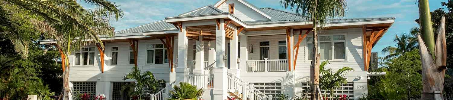A sunny tropical house with a curved driveway, palm trees, and lush landscaping; a white, single-story home with a front porch.
