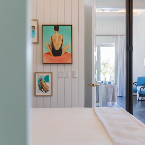 A bright modern room with framed wall art, an open door, and a glimpse of blue chairs through a doorway.
