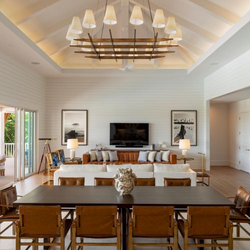 Bright modern living room with dining table, pendant chandelier, sofa, TV, framed wall art, and large sliding doors.