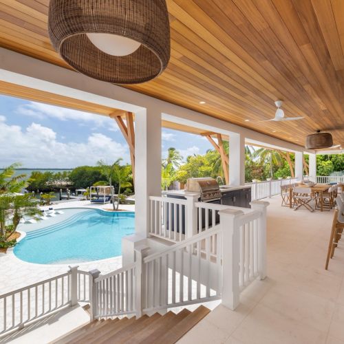 Tropical patio with an infinity pool, palm trees, ocean view, cushioned loungers, a BBQ grill, and hanging ceiling fans.