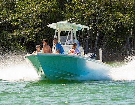 A group of people ride a green speedboat, grinning as it blasts through the water with a splash behind it.